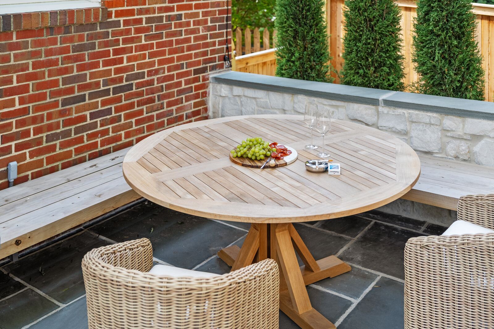 Teak dining table on a bluestone patio inside a stone seat wall