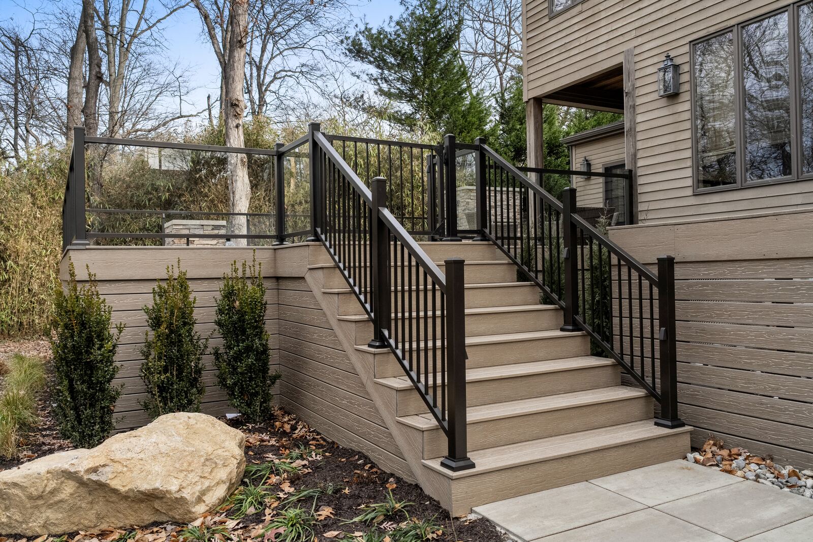 Composite deck stairs with black railings above new arborvitae and boulders