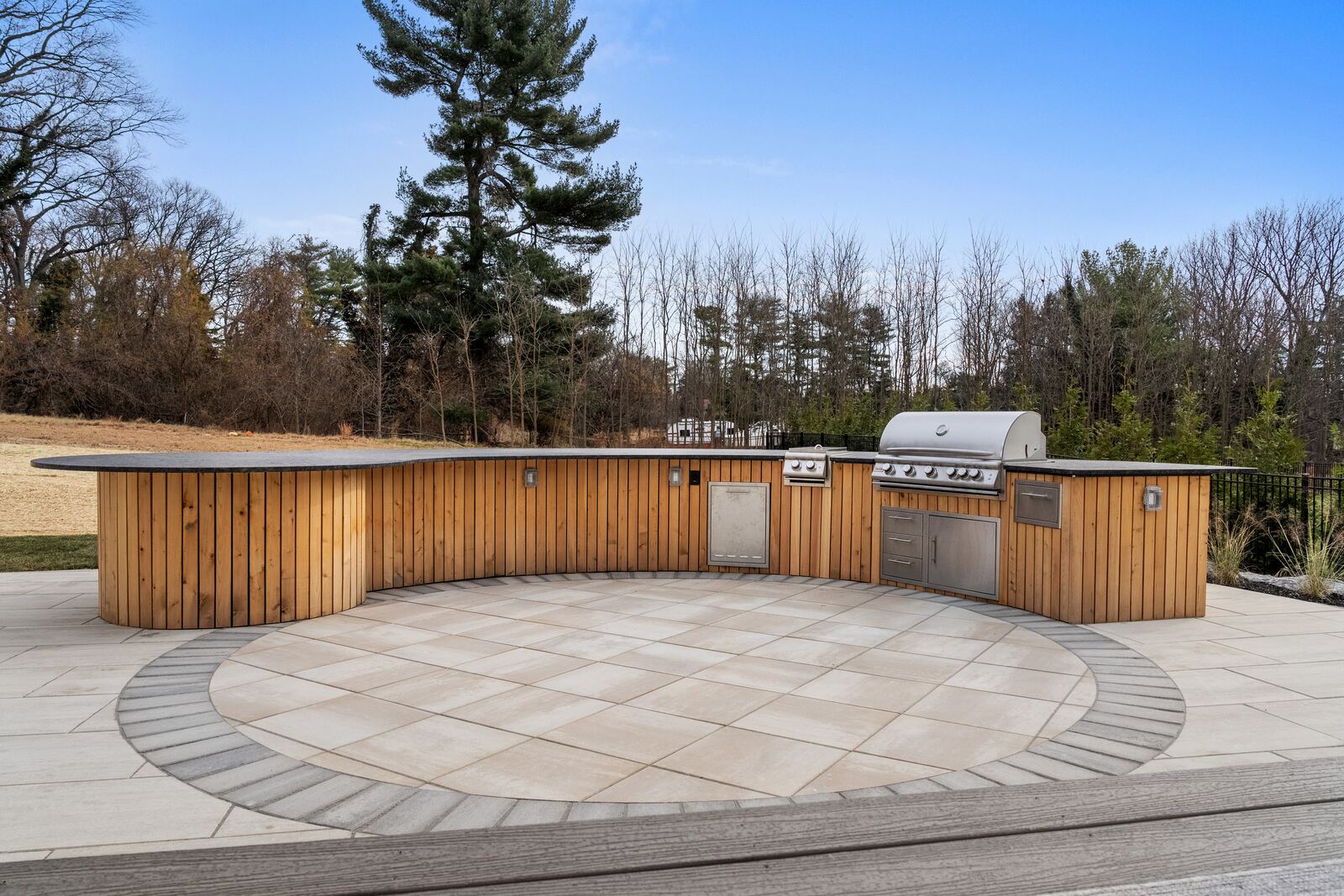 Curved cedar-clad outdoor kitchen with a built-in grill on a porcelain paver patio