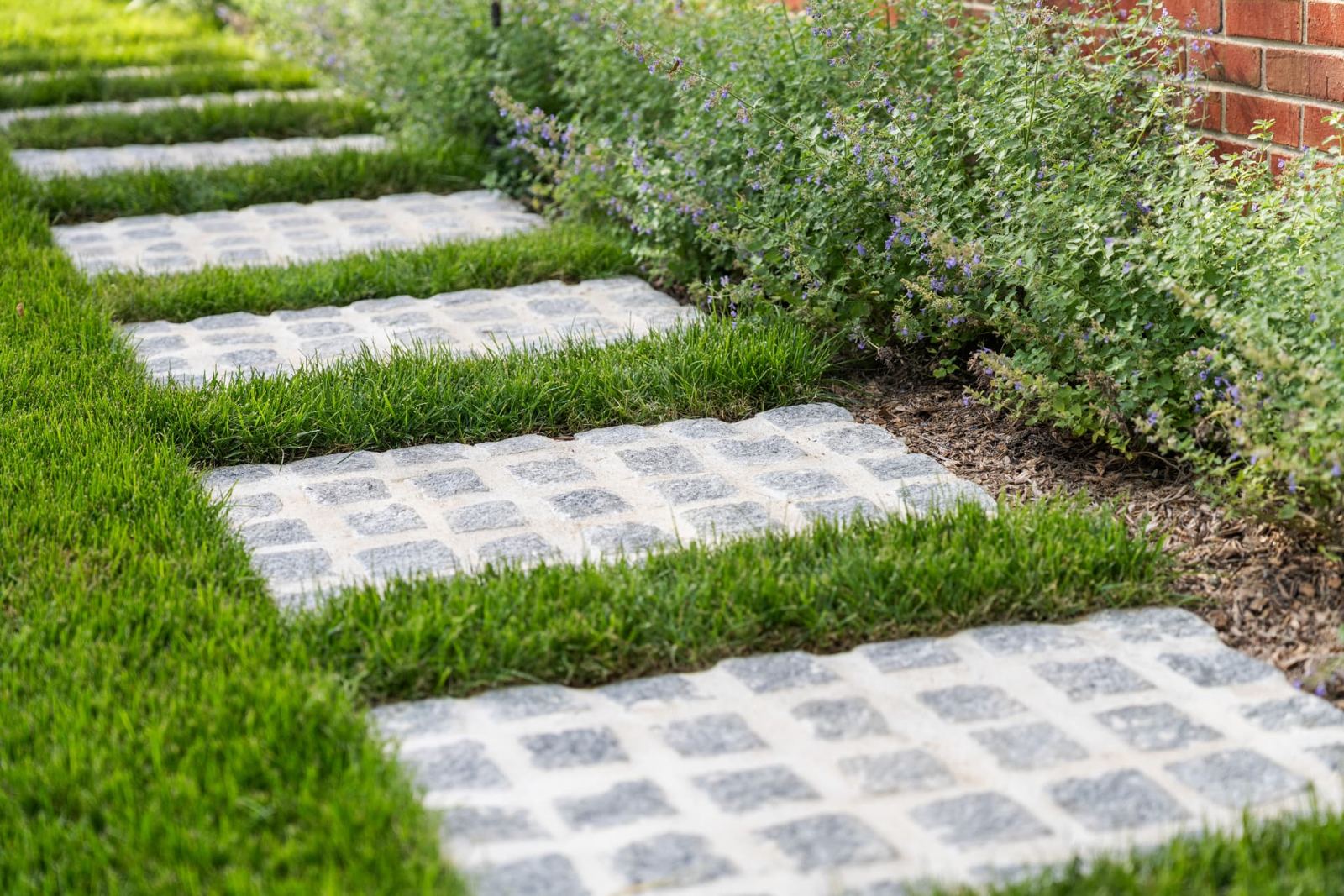 Granite paver steps set in lawn beside a flowering garden bed