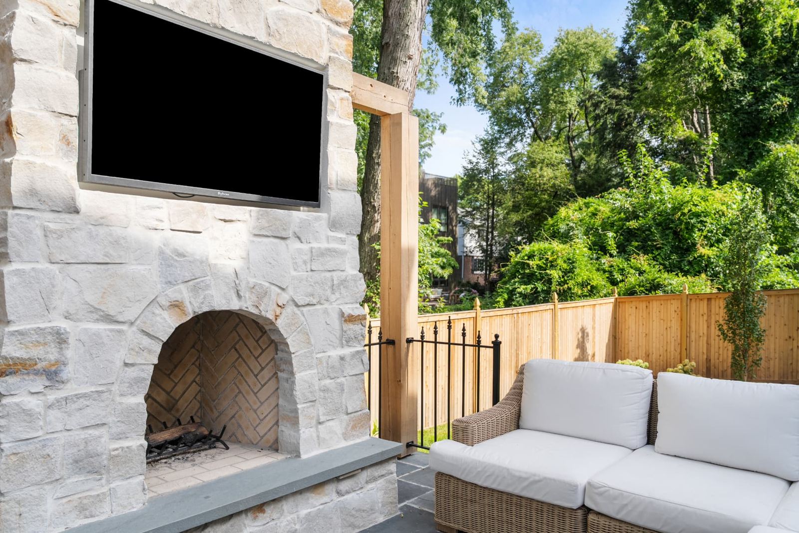 Outdoor lounge with stone fireplace, mounted TV and wicker seating