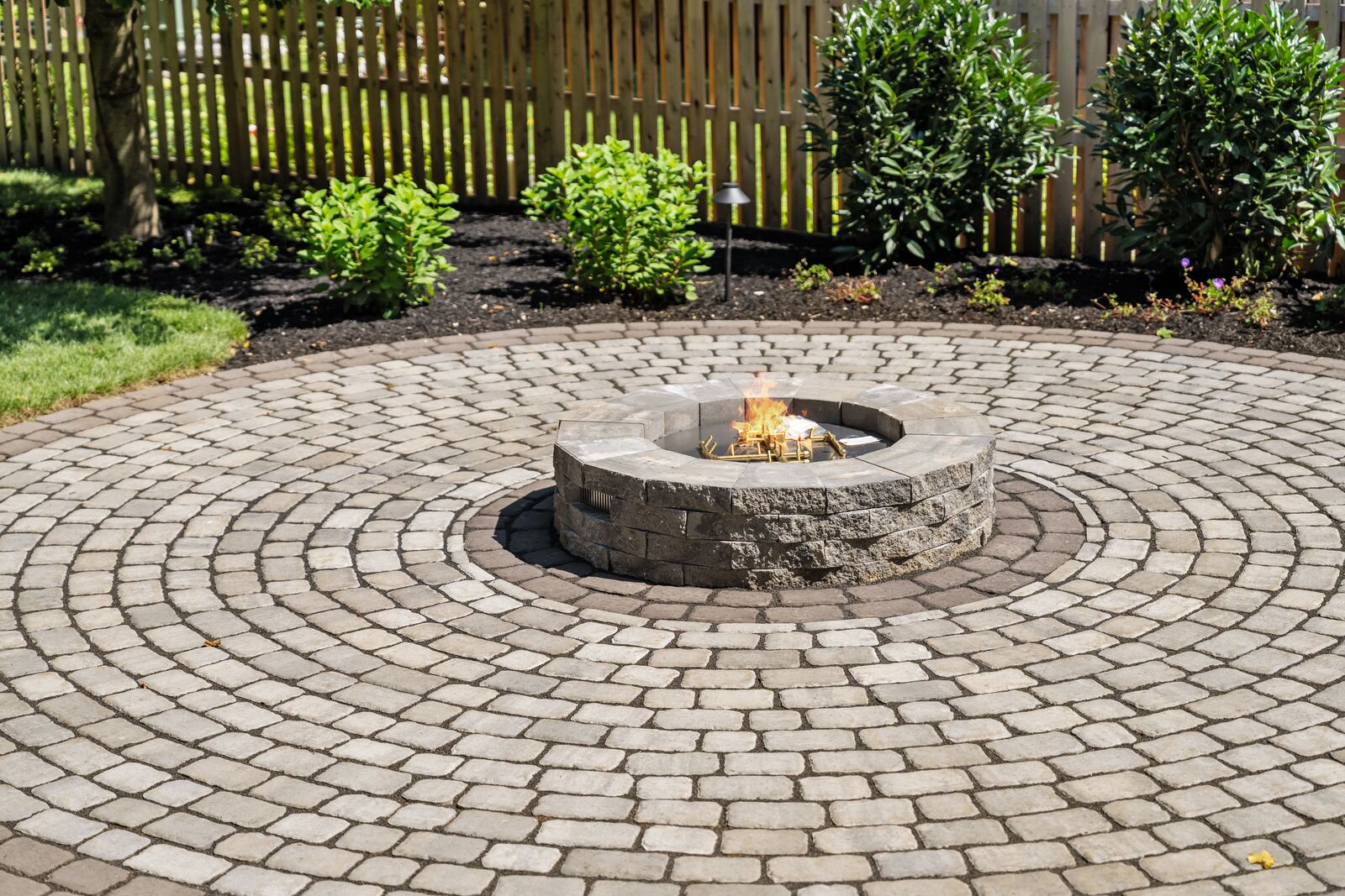 Stone fire pit at the center of a circular paver patio with landscape lighting